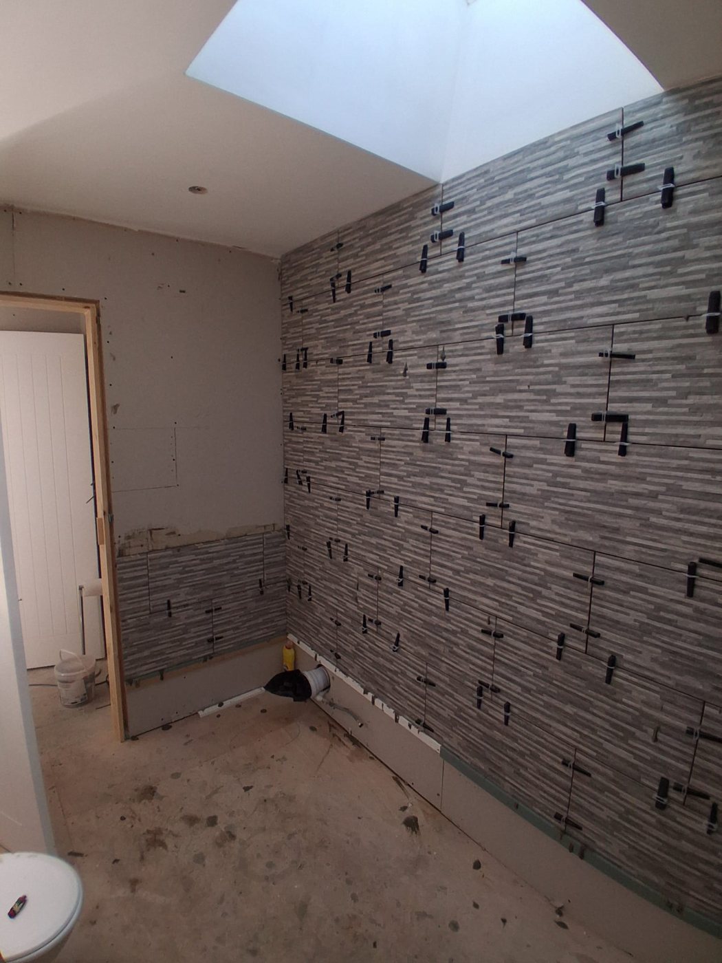 Grey wall tiles part-fitted with levelling clips still in place beneath a rooflight