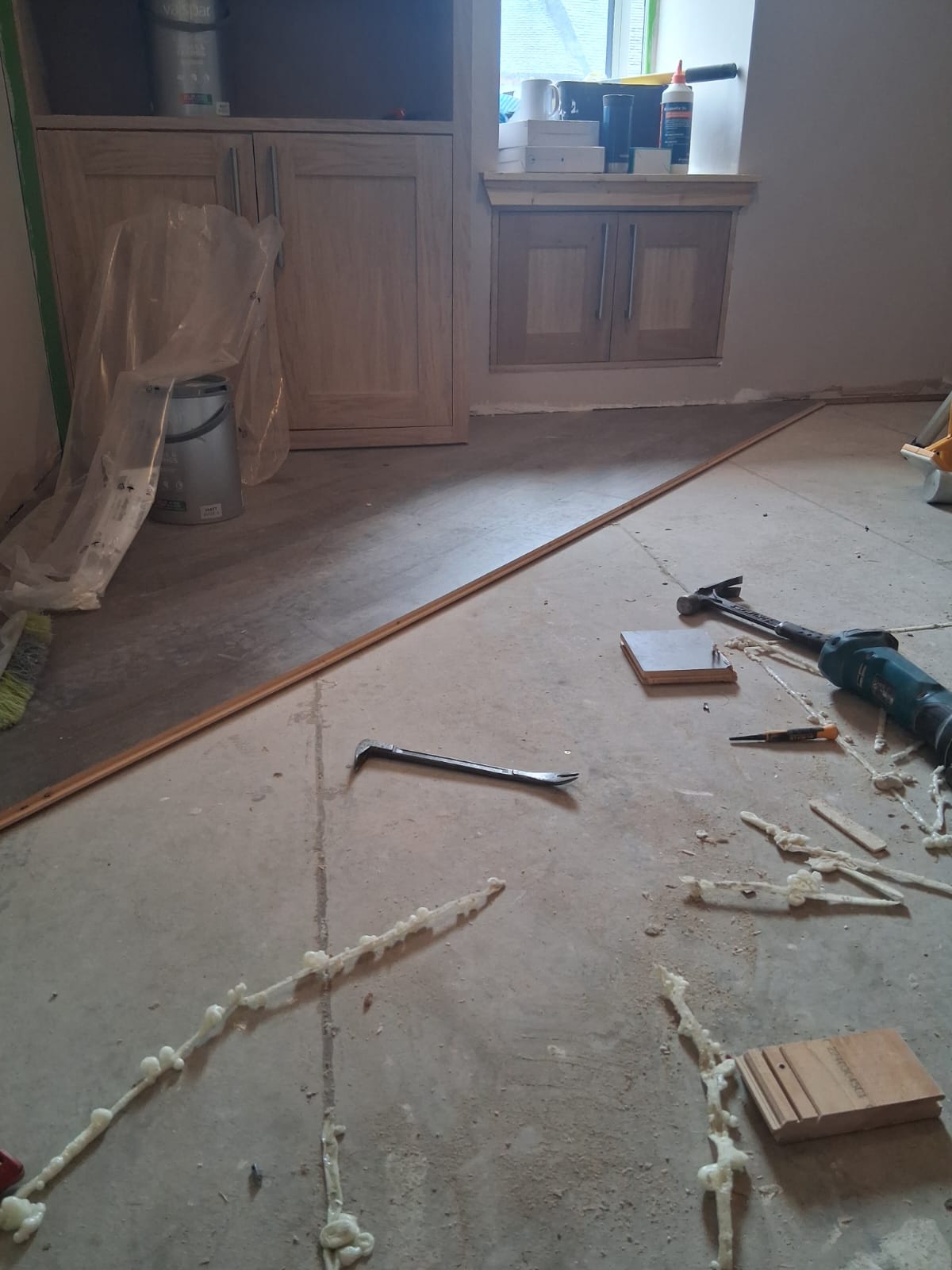 Edge of the part-laid hardwood floor with board offcuts, a hammer and a pry bar on the subfloor