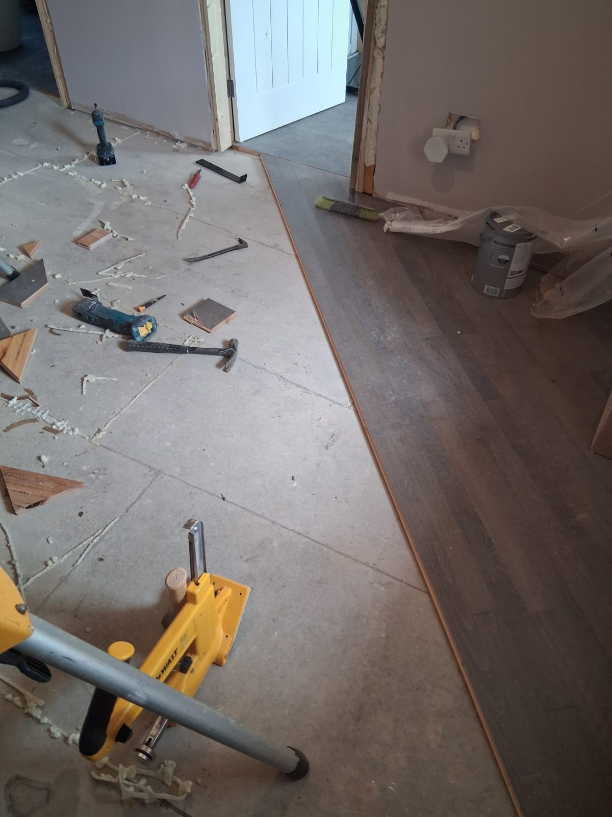 Part-laid hardwood floor running towards a doorway, with a flooring nailer and hand tools on the subfloor
