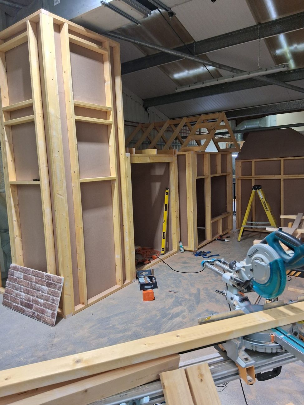 Timber stud walls and a roof truss set out on the workshop floor during the build