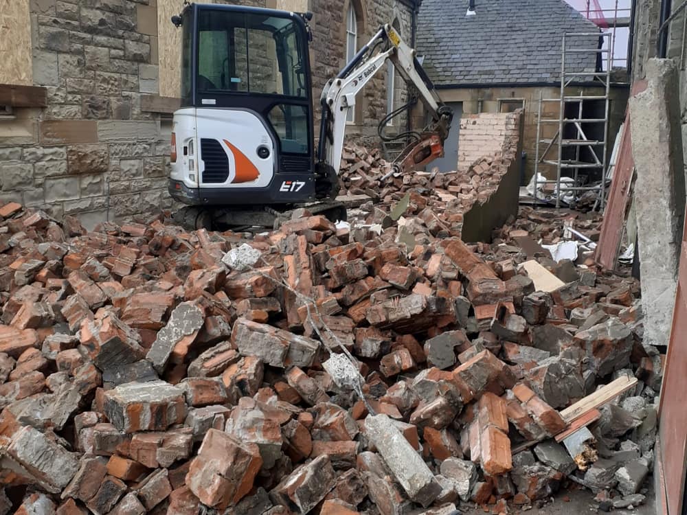 Mini excavator taking down an old brick wall on site