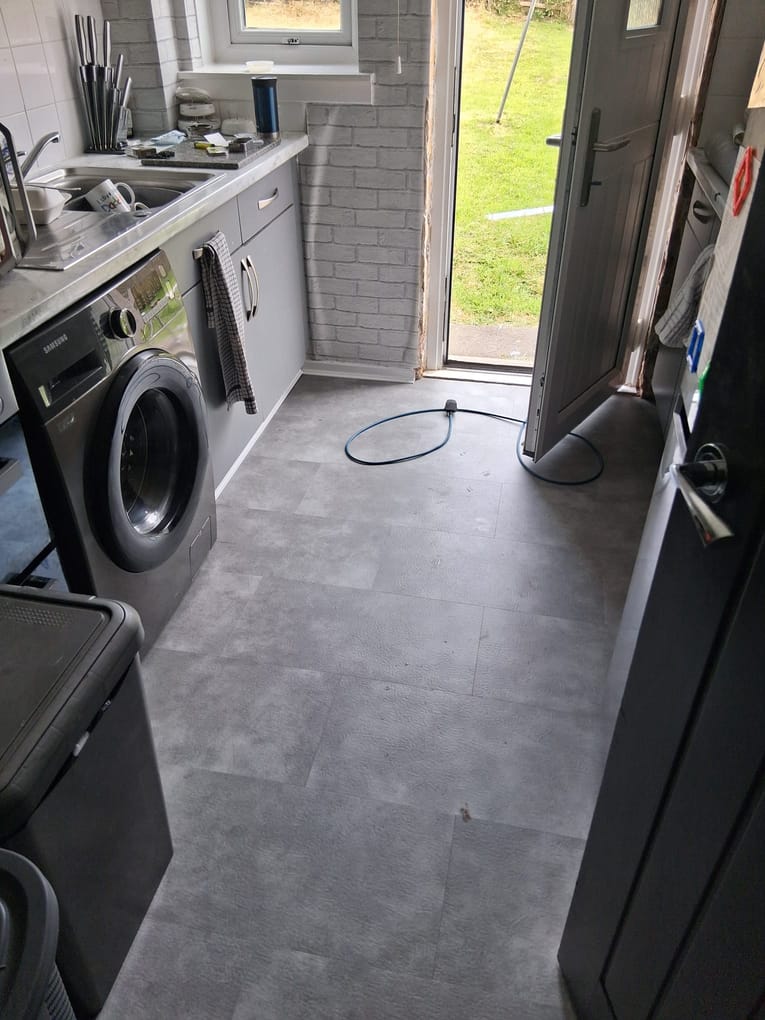Newly laid grey luxury vinyl tile floor in a kitchen with the back door open to the garden